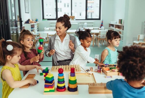 Child Care Center Insurance - Day Care Employee or Kindergarten Teacher Playing with Young Children in the Classroom and Creating Artwork and Building Blocks Together